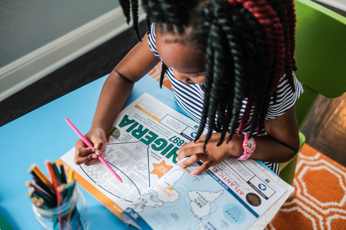 A child colouring the Nigeria 1897 spread at a desk