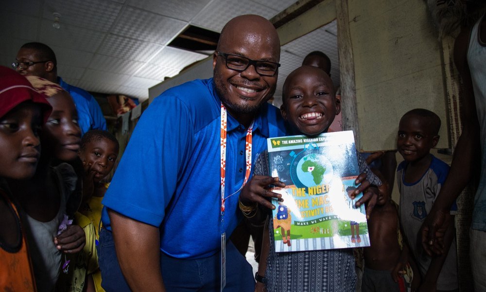 Mobolaji handing a pupil The Nigerian Time Machine Activity Book